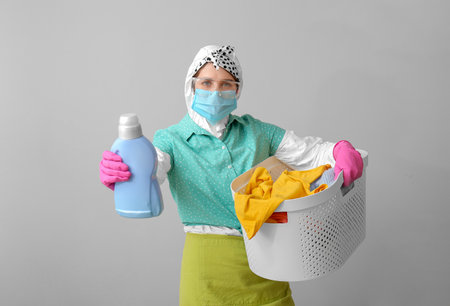 Housewife in protective suit and laundry on gray backgroundの写真素材