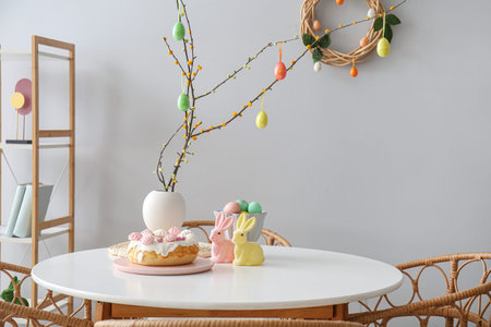 Vase with tree branches, eggs, Easter cake and toy rabbits on table in dining room