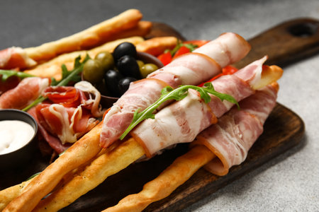 Wooden board of tasty Italian Grissini with bacon on grunge background, closeupの写真素材