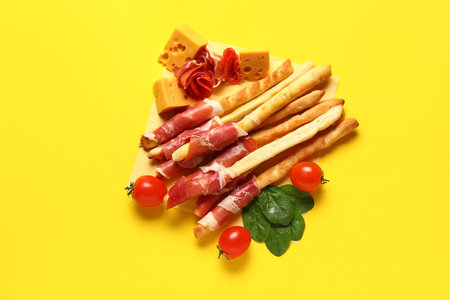 Tasty Italian Grissini with bacon, cheese and tomatoes on yellow backgroundの写真素材