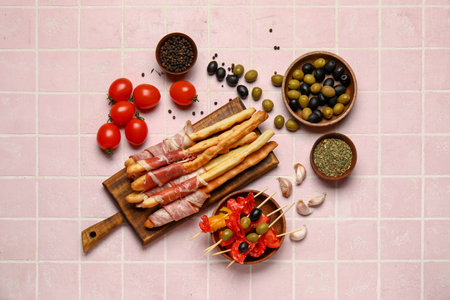 Wooden board of tasty Italian Grissini with bacon, tomatoes and olives on pink tile backgroundの写真素材