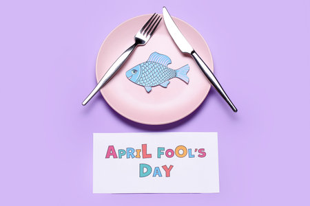 Paper with text APRIL FOOL'S DAY, fish and table setting on lilac backgroundの写真素材