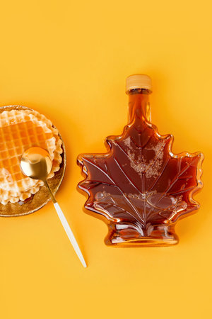 Waffles with bottle and spoon of tasty maple syrup on yellow backgroundの写真素材