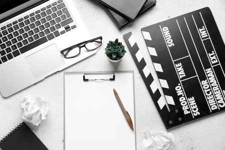 Clipboard with movie clapper, plant, eyeglasses and laptop on white background