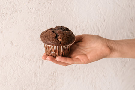 Woman holding tasty chocolate cupcake on light backgroundの写真素材