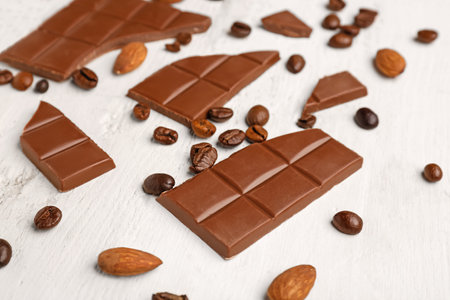 Pieces of tasty chocolate, almonds and coffee beans on light wooden background, closeupの写真素材