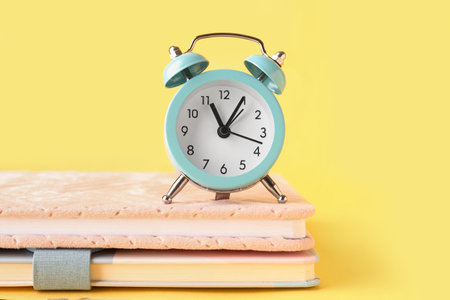 Notebooks and alarm clock on yellow backgroundの写真素材