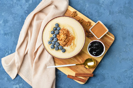 Bowl of tasty semolina porridge with blueberry, cinnamon, nuts and jam on color backgroundの写真素材