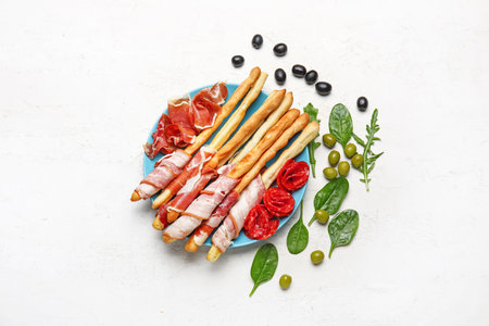 Plate of tasty Italian Grissini with bacon on light backgroundの写真素材