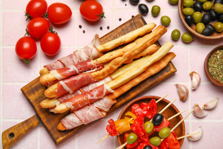 Wooden board of tasty Italian Grissini with bacon on pink tile backgroundの写真素材