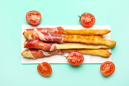Board of tasty Italian Grissini with bacon on turquoise backgroundの写真素材