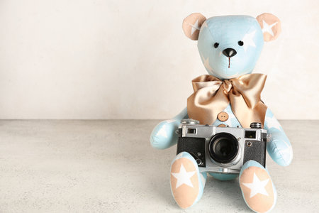 Toy bear with photo camera on table near light wallの写真素材