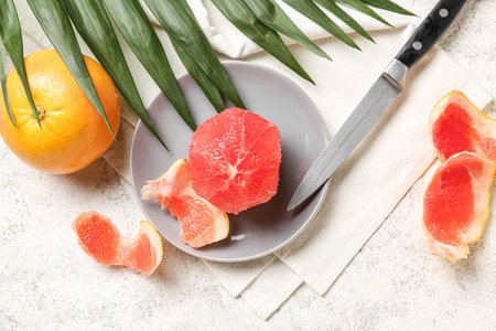 Plate with peeled grapefruit, knife and palm leaf on light backgroundの写真素材