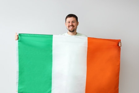 Happy young man with flag of Ireland on light backgroundの写真素材
