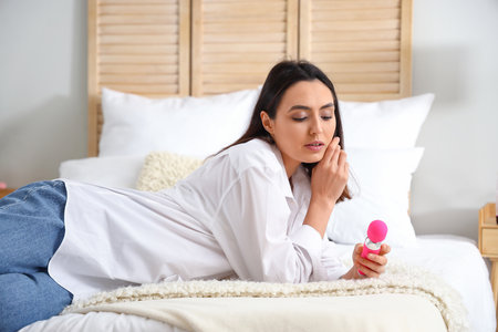 Young woman with vibrator lying on bed at homeの写真素材