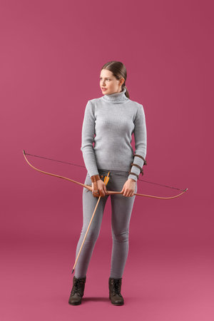 Beautiful woman with crossbow on color background