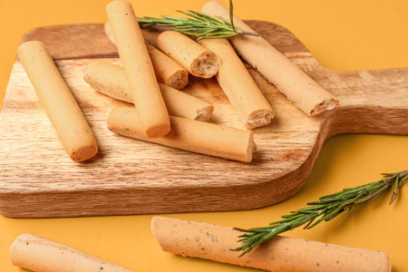Wooden board with tasty Italian Grissini on orange background, closeup