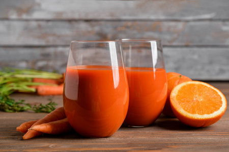 Two glasses of fresh carrot juice and orange on wooden tableの写真素材