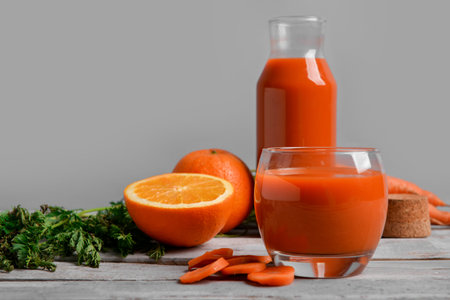 Glass, jug of fresh carrot juice and oranges on gray wooden tableの写真素材
