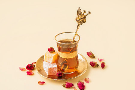 Glass cup of tea with roses and Turkish delight on beige background