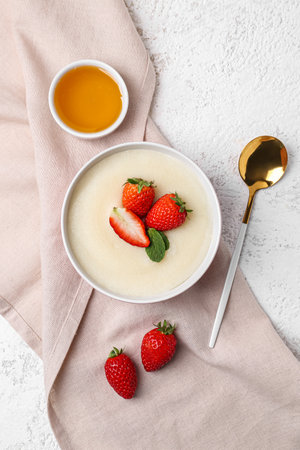 Bowl of tasty semolina porridge with strawberry on light grunge backgroundの写真素材