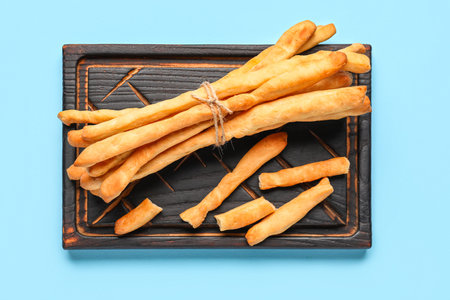 Wooden board with bunch of tasty Italian Grissini on blue background