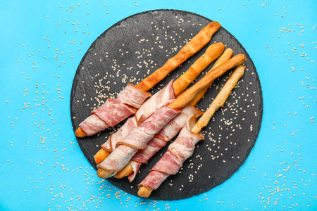 Slate plate of tasty Italian Grissini with bacon on blue backgroundの写真素材