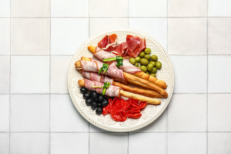 Plate of tasty Italian Grissini with bacon on white tile backgroundの写真素材
