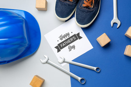 Card with text HAPPY FATHER'S DAY, shoes, hardhat, wooden cubes and wrenches on color backgroundの写真素材