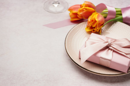 Clean plate, gift box, tulip flowers and wine glass on white grunge tableの写真素材