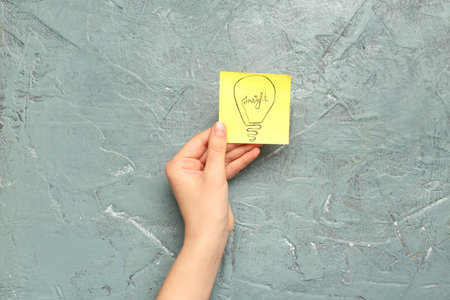Woman holding sticky paper with drawn light bulb on grunge background. insight concept
