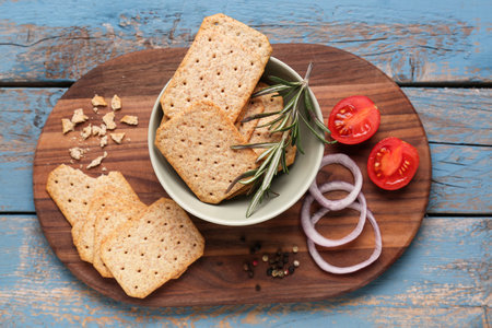 Board with tasty crackers, rosemary, onion and tomatoes on blue wooden backgroundの写真素材