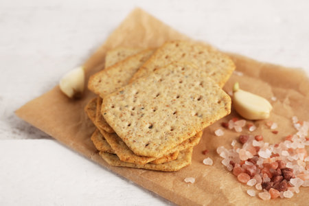 Parchment with stack of tasty crackers, garlic and salt on white wooden backgroundの写真素材