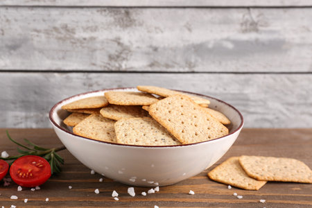 Bowl with tasty crackers, salt, tomatoes and rosemary on wooden tableの写真素材