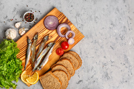 Board with delicious smoked capelin, bread and vegetables on gray grunge backgroundの写真素材