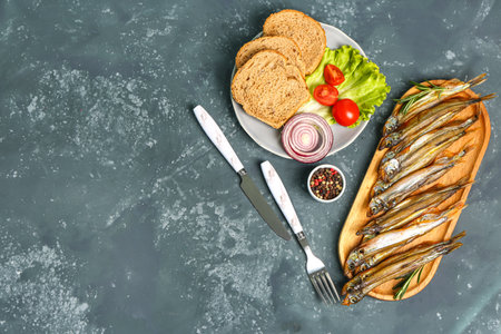 Board with delicious smoked capelin and bread, tomatoes, lettuce, onion on plate against grunge backgroundの写真素材