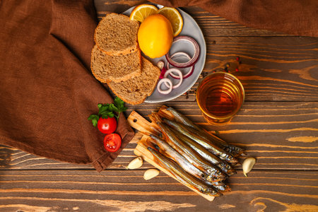 Board with delicious smoked capelin, glass of beer and plate with snacks on wooden backgroundの写真素材
