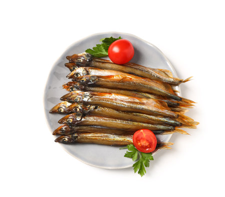 Plate with delicious smoked capelin, tomatoes and parsley isolated on white backgroundの写真素材