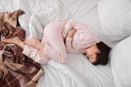 Young woman suffering from menstrual cramps in bedroom, top viewの写真素材