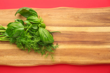 Wooden board with fresh herbs on red background, closeupの写真素材