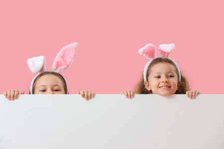Little girls in bunny ears with blank poster on pink background. easter celebrationの写真素材