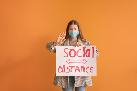Young woman holding paper with text SOCIAL DISTANCE on color background. concept of epidemicの写真素材