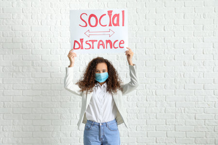Young woman holding paper with text SOCIAL DISTANCE on white brick background. concept of epidemicの写真素材