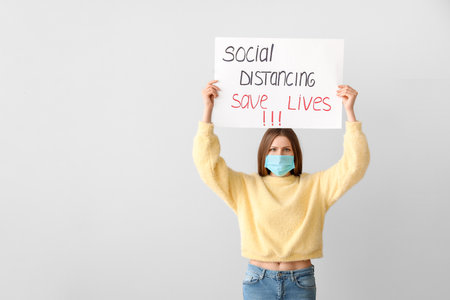 Young woman holding paper with text SOCIAL DISTANCE. SAVE LIVES on gray background. concept of epidemicの写真素材