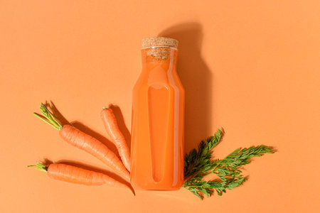 Glass bottle of fresh carrot juice on orange backgroundの写真素材