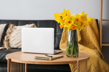 Modern laptop, vase with narcissus flowers and notebook on coffee table in living roomの写真素材