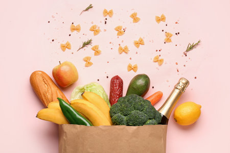 Paper bag with vegetables, fruits and champagne bottle on pink backgroundの写真素材
