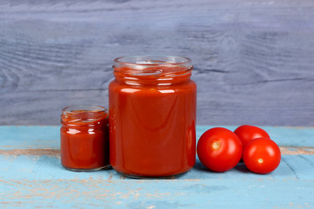 Jars with tasty tomato paste on blue wooden backgroundの写真素材