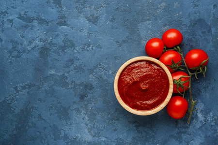 Bowl with tasty tomato paste and fresh vegetables on blue grunge backgroundの写真素材