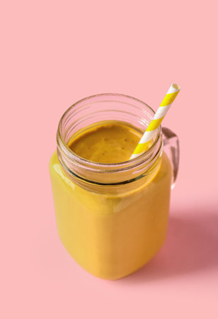 Mason jar of tasty yellow smoothie with straw on pink backgroundの写真素材